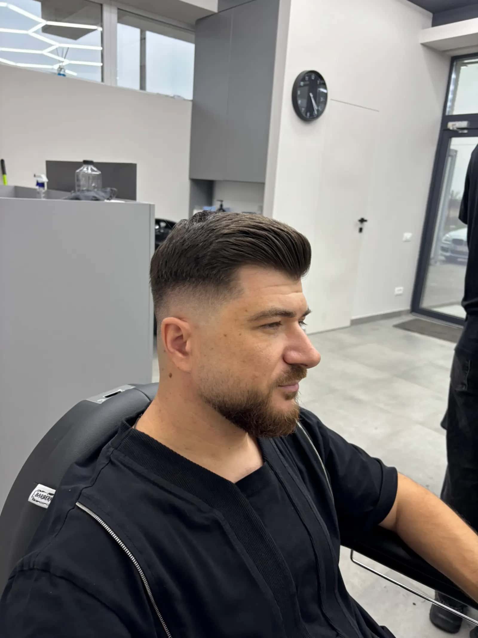 Client din profil cu quiff texturat, mid fade și barbă aranjată